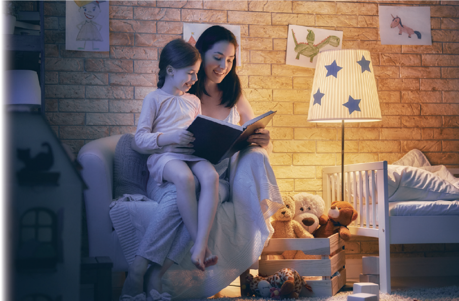 寝室で本の読み聞かせをする母親とそれを聴く子どもの写真